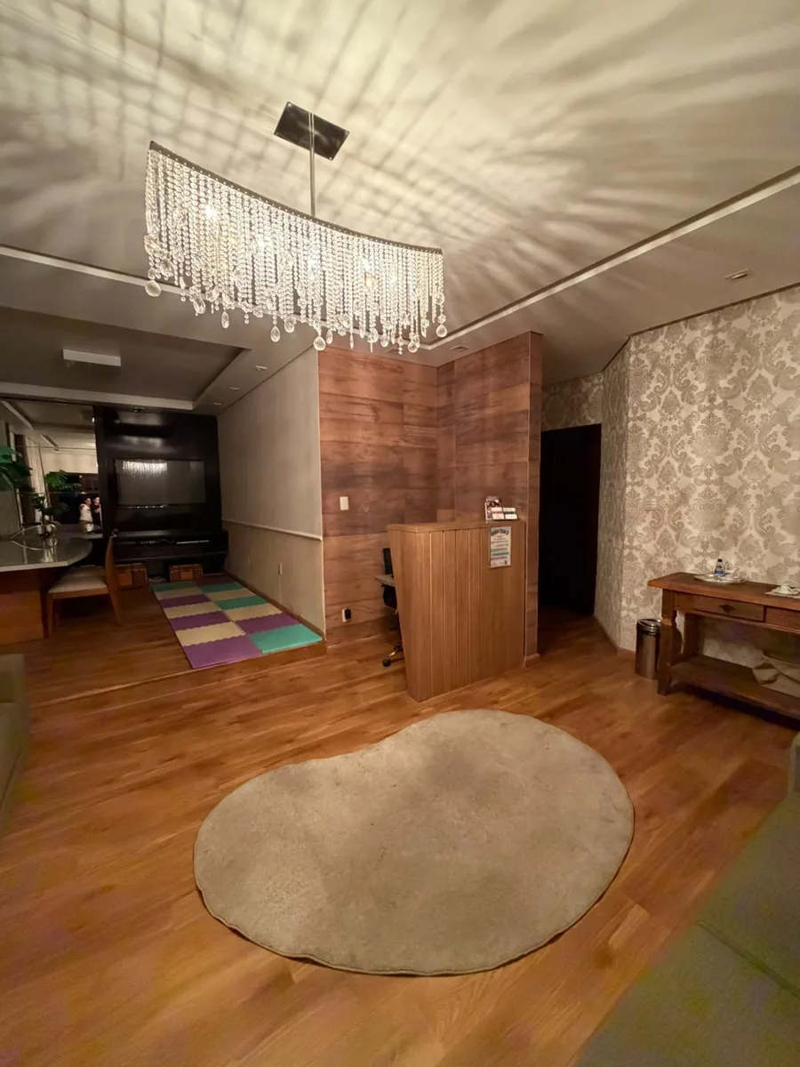 Recepção e sala de espera da clínica pediátrica Diverte e Desenvolve, com lustre de cristal, piso de madeira, tapete redondo e cantinho com tatame colorido para as crianças